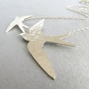 Peut inclure: Un collier en argent avec deux pendentifs en forme d'hirondelle en argent martel&eacute;. Les oiseaux sont reli&eacute;s par une cha&icirc;ne en argent.