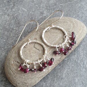 May include: Silver hoop earrings with a hammered finish and dangling garnet gemstones.