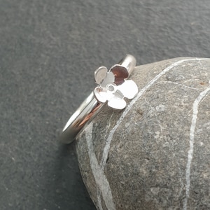 May include: A silver ring with a flower design. The flower is made of three petals and has a small hole in the center.