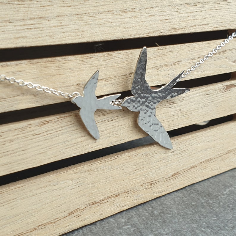 Peut inclure: Un collier en argent avec deux pendentifs en forme d'oiseau en argent martel&eacute;. Les oiseaux se font face et semblent se toucher le bec.