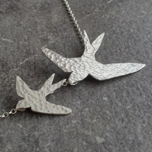 Peut inclure: Un collier en argent avec deux pendentifs en forme d'hirondelle en argent martel&eacute;. Les oiseaux sont tourn&eacute;s dans des directions oppos&eacute;es et sont reli&eacute;s par une cha&icirc;ne en argent.