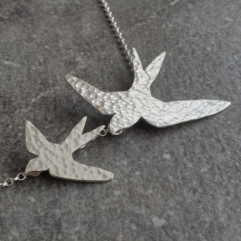 Peut inclure: Un collier en argent avec deux pendentifs en forme d'hirondelle en argent martel&eacute;. Les oiseaux sont tourn&eacute;s dans des directions oppos&eacute;es et sont reli&eacute;s par une cha&icirc;ne en argent.