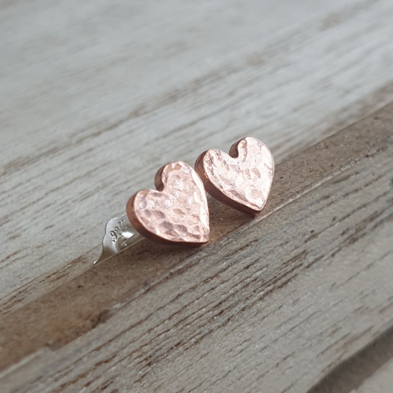 Small heart shaped earrings made from copper which have a dimpled effect across the surface and a shiny finish.