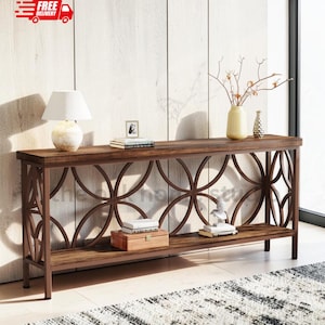 May include: A long rectangular console table with a dark wood finish and a metal frame featuring large circular geometric cutouts on the sides and front. The table has a lower shelf holding a wooden box and books, with a lamp and vase on top.
