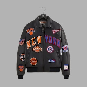 May include: Black leather bomber jacket with multiple patches featuring basketball team logos and the words "NEW YORK" in orange and blue. The jacket has a zip-up front and a ribbed hem and cuffs.