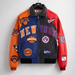 May include: A color-blocked leather jacket with orange, blue, red, and black panels. The jacket features multiple patches and the words "NEW YORK" and "KNICKS" in bold lettering. The jacket has a black collar and cuffs.
