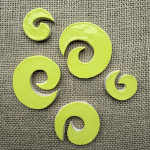 May include: A collection of five lime green ceramic spiral shapes of varying sizes. Each piece features a glossy, smooth finish on the top surface with a white base layer visible along the edges, creating a distinct contrast in color and texture.