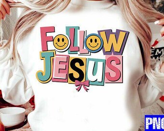 May include: White sweatshirt with the words "Follow Jesus" in colorful, block letters. The design includes smiley faces and a pink bow. The sweatshirt is a casual, comfortable style.