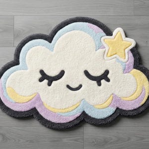 Puede incluir: Una alfombra en forma de nube con una cara sonriente, ojos cerrados y una estrella amarilla. La alfombra presenta un centro blanco, rodeado de acentos pastel azules, amarillos y morados, y un borde gris oscuro. Esta alfombra decorativa es perfecta para una habitación infantil.