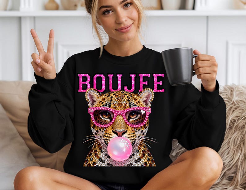 Peut inclure: Un sweat-shirt noir &agrave; col rond avec une impression graphique repr&eacute;sentant un l&eacute;opard portant des lunettes roses scintillantes et faisant une bulle de chewing-gum rose. Le mot BOUJFE est imprim&eacute; en lettres roses scintillantes sur la poitrine.