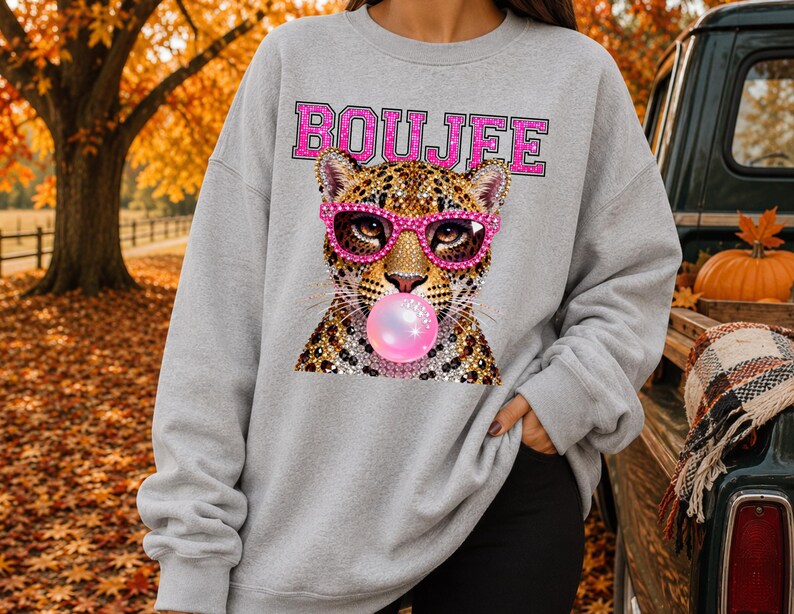 Peut inclure: Un sweat-shirt gris clair &agrave; col rond orn&eacute; d'un motif repr&eacute;sentant un l&eacute;opard portant des lunettes roses &agrave; paillettes et faisant une bulle de chewing-gum rose. Le mot BOUJEE est imprim&eacute; en lettres majuscules roses &agrave; paillettes.