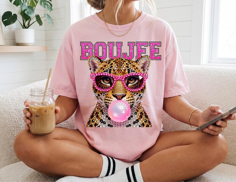 Peut inclure: Un t-shirt rose clair avec un motif repr&eacute;sentant un l&eacute;opard portant des lunettes roses style strass et faisant une bulle de chewing-gum rose. Le mot BOUJFE est imprim&eacute; en grandes lettres majuscules roses et scintillantes au-dessus du l&eacute;opard.