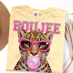 Peut inclure: Un t-shirt jaune clair avec un motif repr&eacute;sentant un l&eacute;opard portant des lunettes rose vif et faisant une bulle de chewing-gum rose. Le mot BOUJEE est imprim&eacute; en grandes lettres majuscules roses &agrave; effet paillet&eacute; au-dessus du l&eacute;opard.