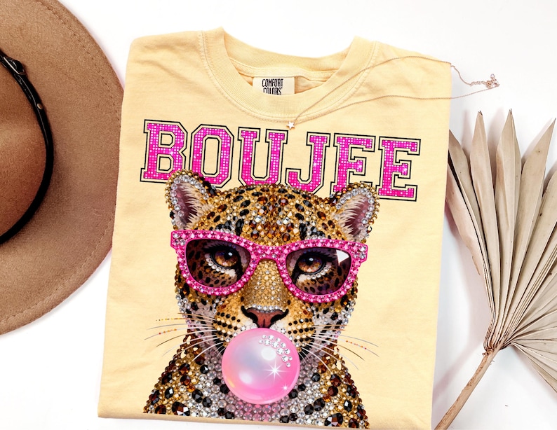 Peut inclure: Un t-shirt jaune clair avec un motif repr&eacute;sentant un l&eacute;opard portant des lunettes rose vif et faisant une bulle de chewing-gum rose. Le mot BOUJEE est imprim&eacute; en grandes lettres majuscules roses &agrave; effet paillet&eacute; au-dessus du l&eacute;opard.