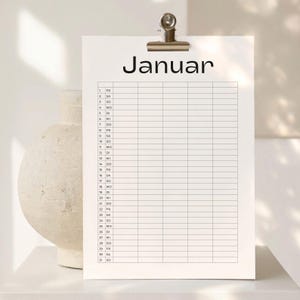 May include: A white paper calendar sheet for the month of Januar with black text and a grid layout. The calendar is held by a silver metal clip at the top. The page lists numbers one through thirty-one with corresponding days of the week.