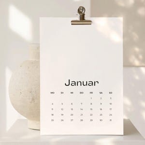 May include: A white wall calendar page for the month of Januar with black text and numbers. The calendar is held by a silver metal binder clip at the top. The days of the week are listed as MO, DI, MI, DO, FR, SA, SO, with dates ranging from 1 to 31.