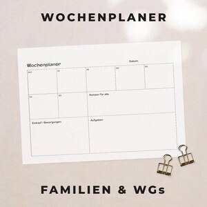 May include: A white weekly planner with the German text "Wochenplaner" at the top and the bottom. The planner has sections for each day of the week, notes, shopping, and tasks. Two gold binder clips are in the bottom right corner.