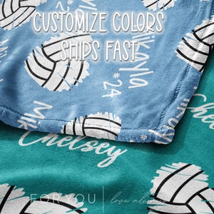 May include: A close-up of a blue and teal blanket with volleyball graphics. The blanket has white text that says "Customize Colors Ships Fast". The blanket also has personalized names and numbers.