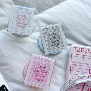 May include: Three rectangular acrylic blocks and one pink rectangular item, each featuring a printed library card design with the text "LIBRARY CARD" and "Sorry, I'm fully booked tonight!" in various colors including red, black, and pink.