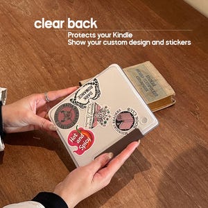 May include: A clear Kindle case with a textured surface, decorated with various stickers including text that reads "Dark Romance," "Hot and Spicy," and "Midnight Readers Book Club." The case features text stating "clear back" and "Protects your Kindle."