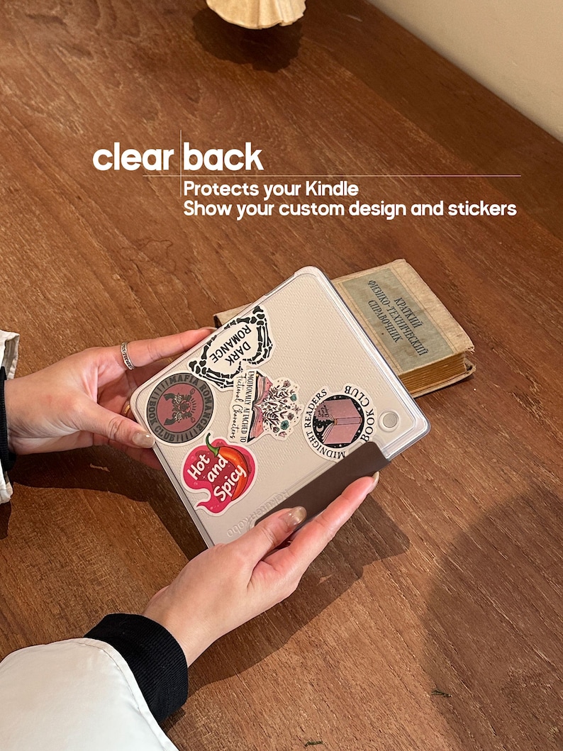 May include: A clear Kindle case with a textured surface, decorated with various stickers including text that reads "Dark Romance," "Hot and Spicy," and "Midnight Readers Book Club." The case features text stating "clear back" and "Protects your Kindle."