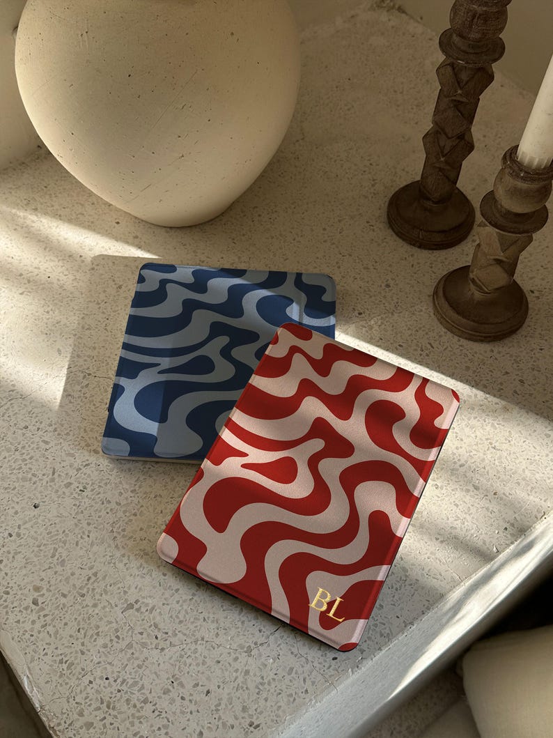 Puede incluir: Dos tarjeteros rectangulares con patrones ondulados. Uno es rojo con remolinos blancos, el otro es azul con remolinos azul oscuro. El tarjetero rojo tiene las iniciales doradas "BL".