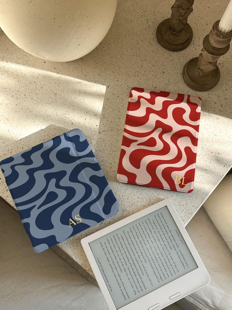 Puede incluir: Tres fundas decorativas para lectores electr&oacute;nicos con dise&ntilde;os ondulados. Una es azul con remolinos azul oscuro e iniciales doradas "AS". Otra es roja y blanca, con iniciales doradas "BL". Tambi&eacute;n se ve un lector electr&oacute;nico blanco.