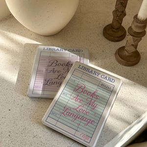 Books Are My Love Language library card Kindle case on a cozy coffee table with candle decor, vintage reader aesthetic cover for Kindle Paperwhite, personalized bookish Kindle case gift for readers and book lovers.