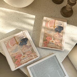 May include: Three decorative card cases with floral and sword designs, featuring the names "Rose" and "Eliza" and the text "You do not yield." A white e-reader is also present, displaying text on its screen.