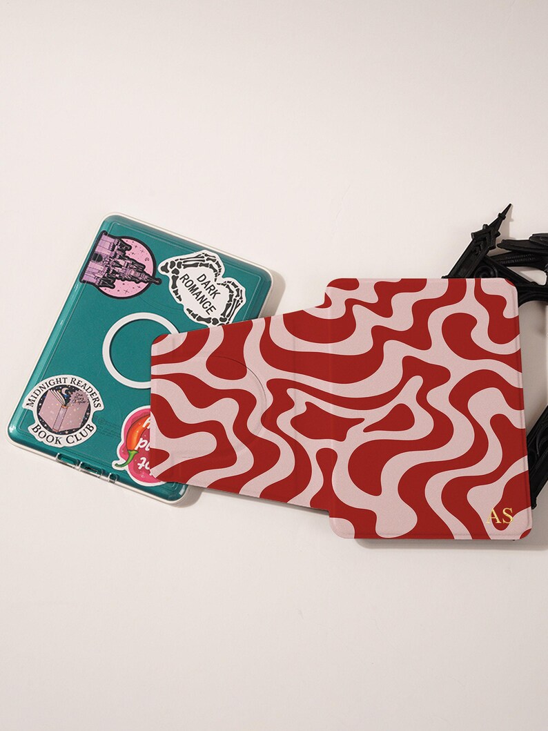 Puede incluir: Una funda para port&aacute;til de color turquesa con pegatinas y un tarjetero con un patr&oacute;n ondulado rojo y rosa. Las pegatinas incluyen "Dark Romance" y "Midnight Readers Book Club". El tarjetero tiene las iniciales "AS".