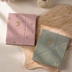 May include: A pink tablet case and a sage green tablet case, both featuring gold-colored moon and star accents. The sage green case includes the gold-colored letters AS in the bottom right corner. Both cases have a smooth, matte finish.