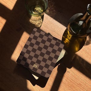 Chocolate checkerboard Kindle case resting on a book by the window, minimal bookish scene with natural light and quiet reading atmosphere