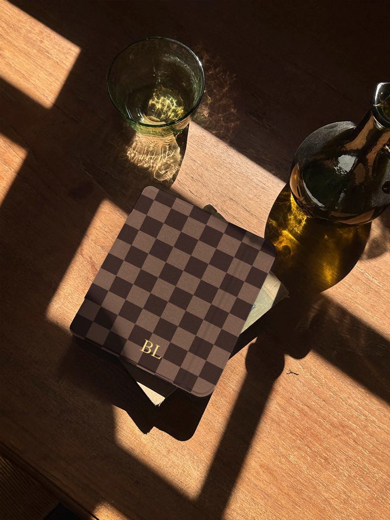 Chocolate checkerboard Kindle case resting on a book by the window, minimal bookish scene with natural light and quiet reading atmosphere