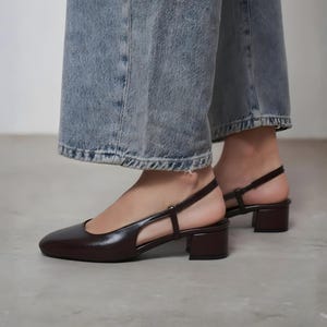Może przedstawiać: Bordowe skórzane buty typu slingback na niskim obcasie. Buty mają szpiczasty nosek i pasek wokół kostki. Noszone z niebieskimi dżinsami.