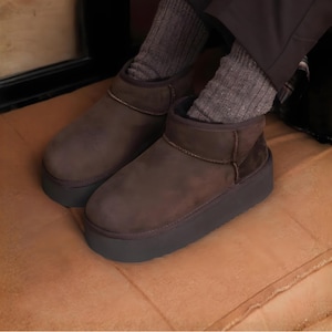 May include: Brown platform boots with a dark gray sole. The boots have a suede-like texture and a short ankle height. The boots are worn with gray ribbed socks.