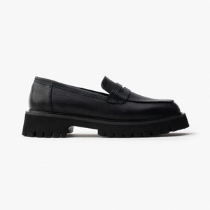 May include: Black leather loafer with a chunky, lug sole. The shoe features a classic penny loafer design with a textured leather upper and a low heel. The sole is thick and has a rugged tread for added grip. A stylish and comfortable shoe.