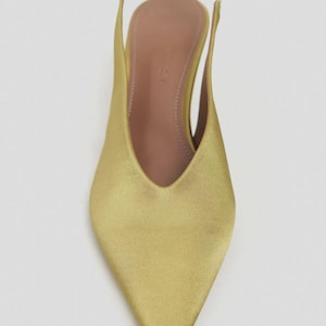 Może przedstawiać: But typu slingback ze szpiczastym noskiem w metalicznym, chartreuse satynowym wykończeniu. But posiada głębokie wycięcie w kształcie litery V, smukły obcas oraz dopasowany elastyczny pasek na pięcie. Wkładka wewnętrzna jest w neutralnym kolorze beżowym.
