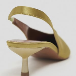 Może przedstawiać: Satinowy but typu slingback w kolorze chartreuse ze szpiczastym noskiem i niskim, rozszerzanym obcasem typu kaczuszka. But posiada cienki, elastyczny pasek na pięcie, dopasowaną satynową zapiętkę oraz jasną wkładkę z widocznym przeszyciem.