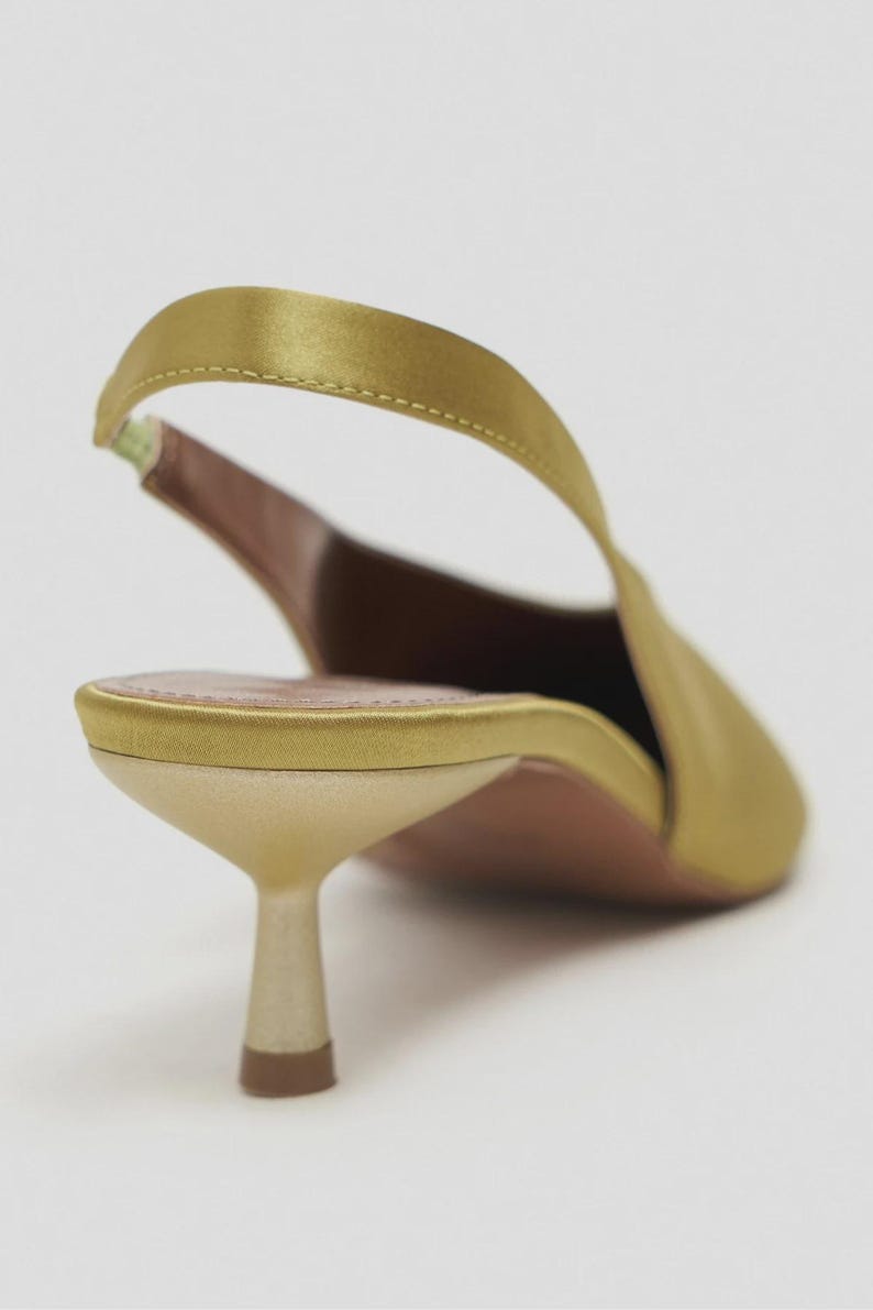 Może przedstawiać: Satinowy but typu slingback w kolorze chartreuse ze szpiczastym noskiem i niskim, rozszerzanym obcasem typu kaczuszka. But posiada cienki, elastyczny pasek na pięcie, dopasowaną satynową zapiętkę oraz jasną wkładkę z widocznym przeszyciem.