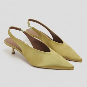 Może przedstawiać: Para but&oacute;w typu slingback z satyny w kolorze chartreuse, ze szpiczastym noskiem, niskim obcasem typu kaczuszka oraz jasnozielonym elastycznym paskiem na pięcie. Wnętrze but&oacute;w wyłożone jest brązowym materiałem, o smukłym i prostym kroju.