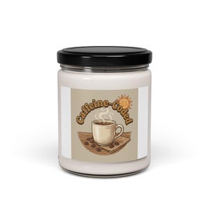 Puede incluir: Un tarro de vela blanco con tapa negra. La etiqueta presenta una taza de café con vapor, granos de café y las palabras "Caffeine-Coded" en una fuente retro, con un gráfico de sol. La vela es probablemente perfumada.
