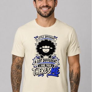 May include: A cream-colored short-sleeve t-shirt featuring a graphic of a black sheep. The text reads: A LITTLE DIFFERENT... A LOT DIFFERENT... AND THEN THERE'S ME. The design uses black and blue lettering with blue accents around the sheep.
