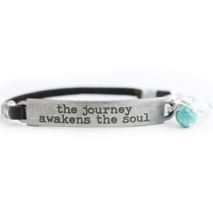 May include: A brown leather bracelet with a silver charm that reads "the journey awakens the soul". The charm has a turquoise bead attached to it.