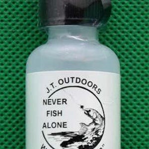 May include: A small, clear bottle of silicone gel floatant for fishing. The bottle has a black cap and a white label with the text "J.T. Outdoors NEVER FISH ALONE WATER 'WALKER' SILICONE GEL FLOATANT" and a graphic of a fish.