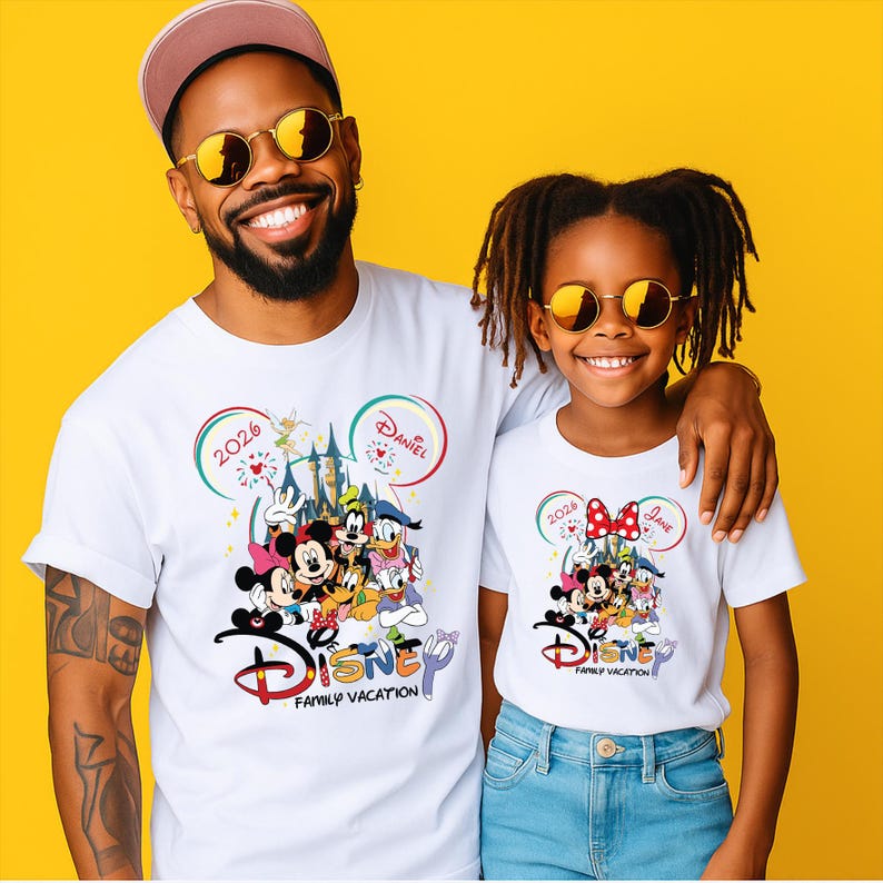 Puede incluir: Camisetas blancas con un dise&ntilde;o de Vacaciones Familiares de Disney. Las camisetas muestran un gr&aacute;fico colorido de personajes de Disney, un castillo y el texto "2026 Daniel" y "2026 Jane". Las camisetas son usadas por una persona y un ni&ntilde;o.