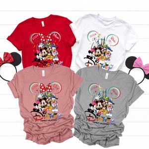 Puede incluir: Cuatro camisetas de manga corta de Disney para vacaciones familiares en rojo, blanco, rosa y gris. Cada camiseta presenta un gr&aacute;fico de personajes de Disney con el texto "2026" y un nombre. El logotipo de Disney y "Family Vacation" est&aacute;n impresos en la parte inferior.