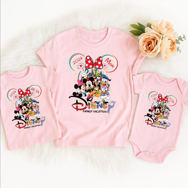 Puede incluir: Camisetas rosas y un body con un dise&ntilde;o de vacaciones familiares de Disney. Las camisetas tienen un gr&aacute;fico de Mickey Mouse, Minnie Mouse y otros personajes de Disney. El texto incluye "2026" y "Mam&aacute;".