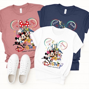 Puede incluir: Tres camisetas en rosa, blanco y azul marino con gr&aacute;ficos de personajes de Disney. Cada camiseta presenta orejas de Mickey Mouse, el a&ntilde;o "2026" y las palabras "Disney Family Vacation". Zapatillas blancas en primer plano.