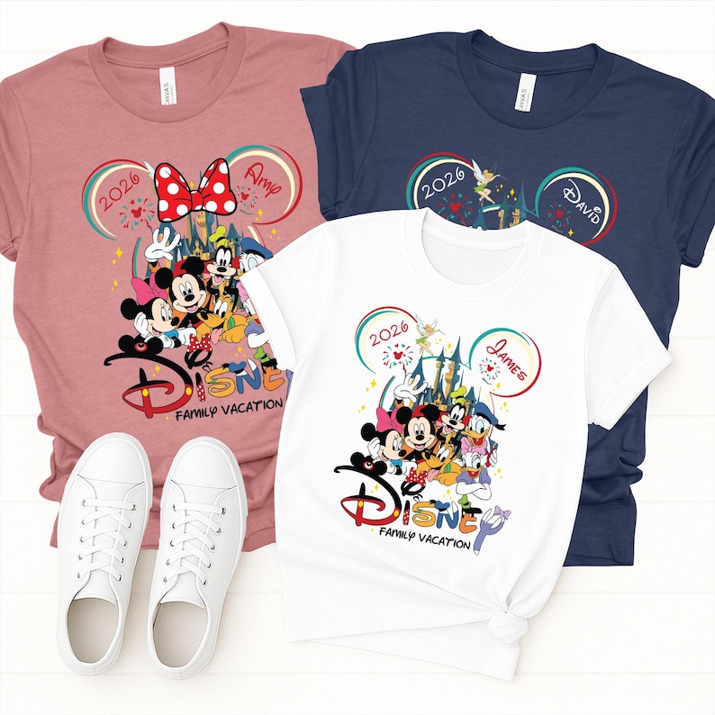 Puede incluir: Tres camisetas en rosa, blanco y azul marino con gr&aacute;ficos de personajes de Disney. Cada camiseta presenta orejas de Mickey Mouse, el a&ntilde;o "2026" y las palabras "Disney Family Vacation". Zapatillas blancas en primer plano.