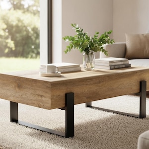 May include: A rectangular coffee table featuring a thick, light brown wood-grain top and sturdy black metal U-shaped legs. The table surface holds a small white ceramic mug on a saucer, a stack of books, and a clear glass vase with green leaves.